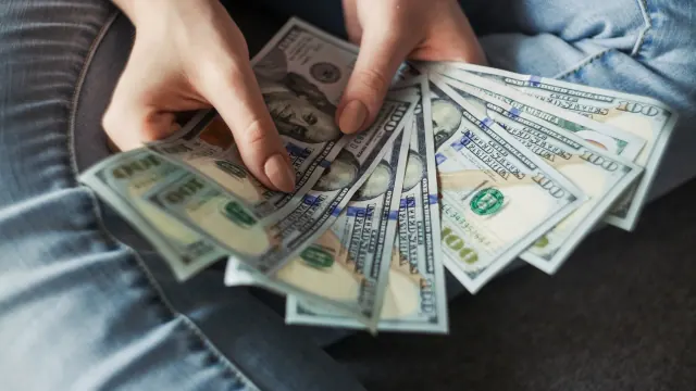 Hands fan out dollar bills on a table for best ways to save 1000 fast.