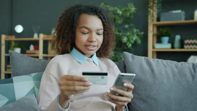 A woman checks a card and phone for how much spending money a week is reasonable.