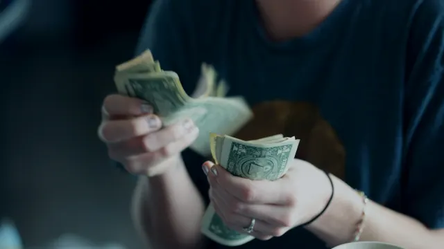 A person counts a handful of cash while learning how to quickly save money.