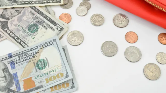 Bills and coins spread beside a red folder for a money saving book with envelopes.