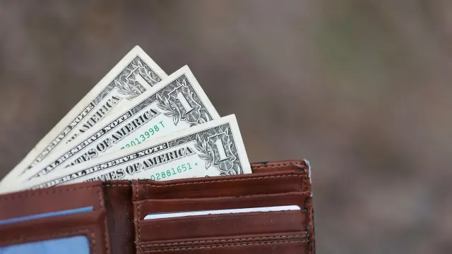 Cash tucked into a wallet suggests using money saving envelopes.