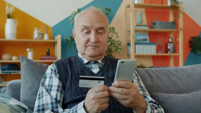 An older man checks a card and phone while practicing financial discipline.