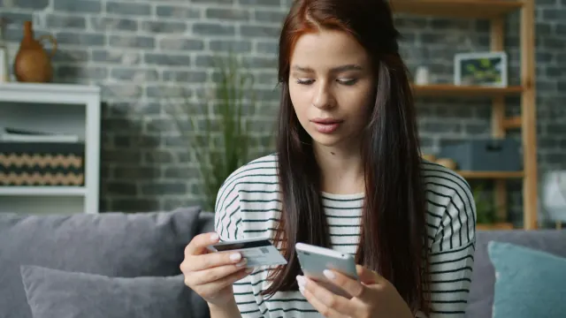 A woman comparing two cards on her phone while asking why cant I save money.