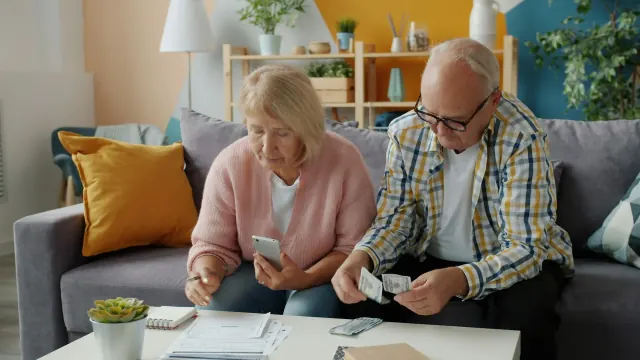 An older couple sorts cash and papers while manually saving their money.